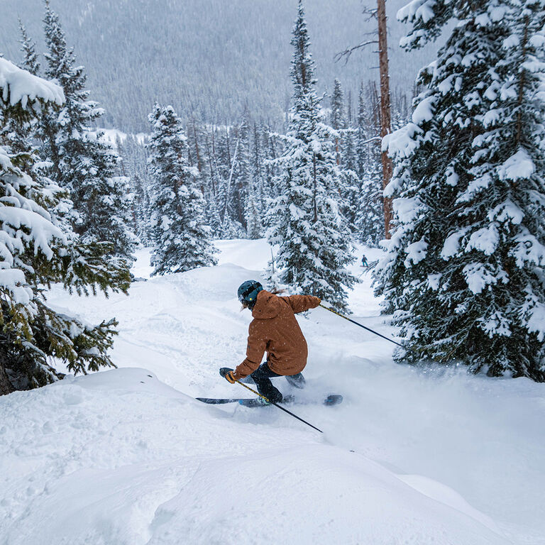 woman skiing through trees and powder